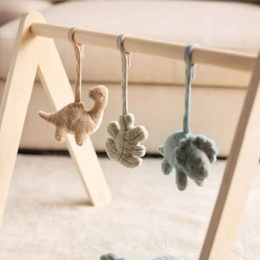 Plush dinosaur toys hanging on a wooden baby gym.